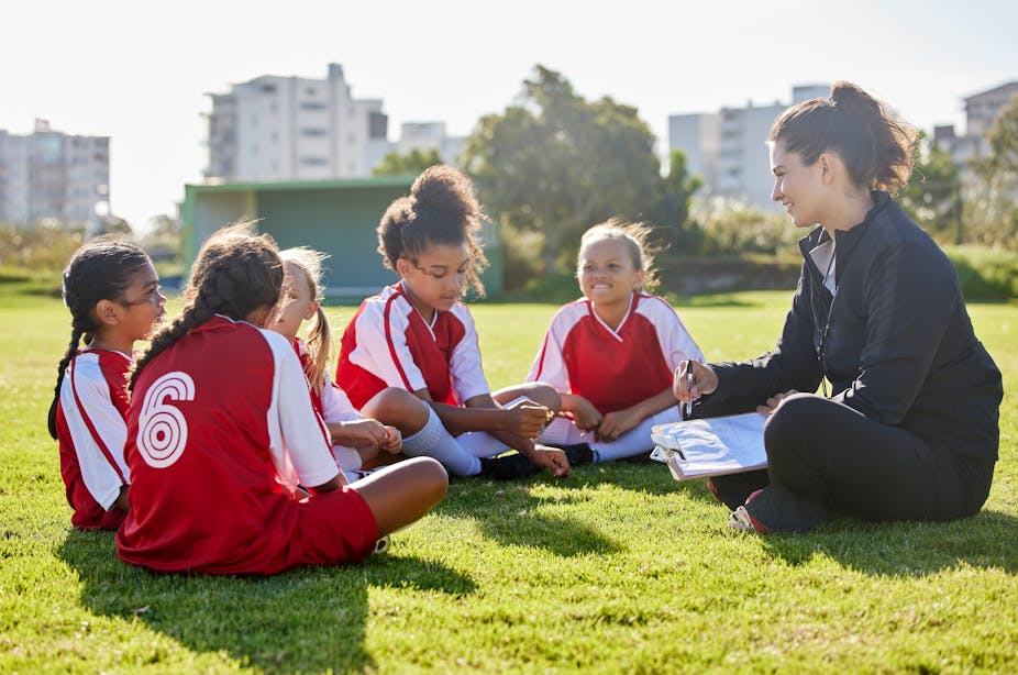 A group of girls wearing football uniforms sit with their female coach.