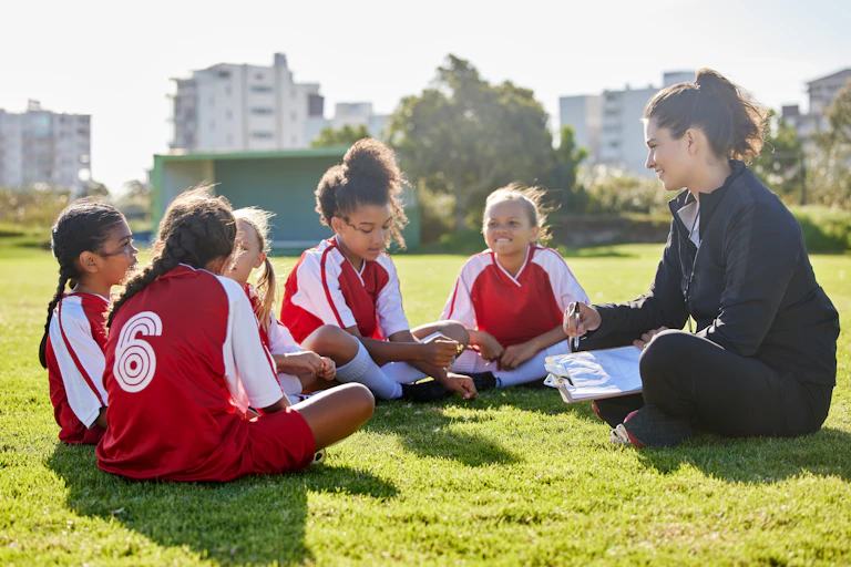 A group of girls wearing football uniforms sit with their female coach.