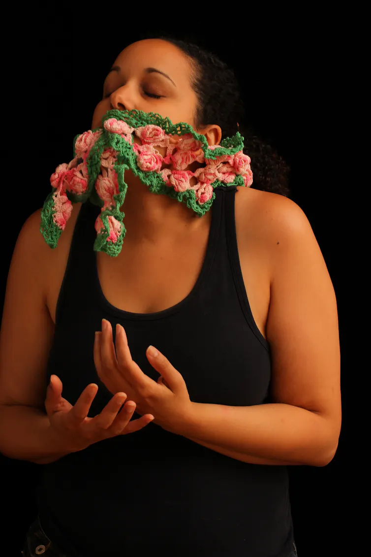 A figure seen with crocheted flowers appearing to emerge from the mouth.