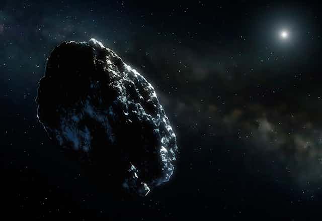 An oval-shaped gray and black asteroid against a cloudy, starry space background, with a bright star in the top right corner. 