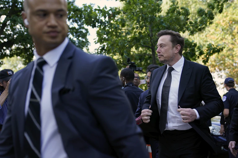 Man in suit walks outside while holding lapels of his suit.
