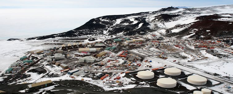 An overhead view of a research station comprised of several buildings, including four circular white ones. The landscape is covered in snow and there's a brown hill in the background.