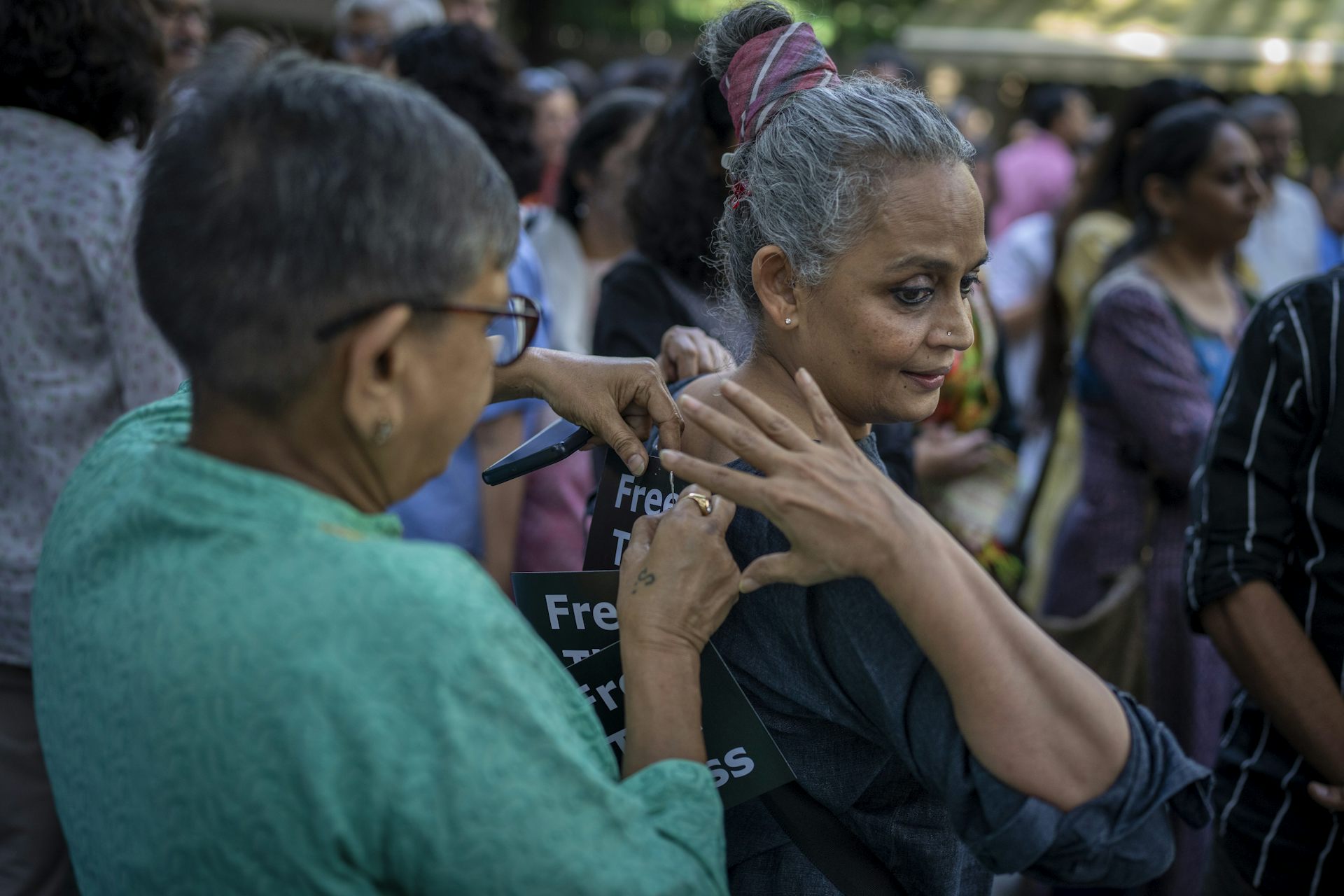 A woman in a green shirt pins a placard on the dress of a grey-haired woman.
