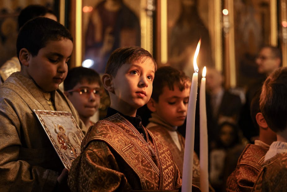 Children, dressed in robes and holding candles, pray at a church.