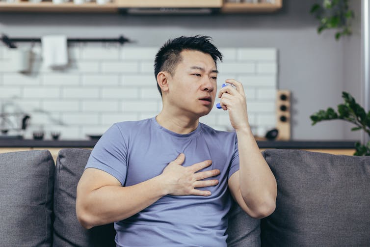 A man sitting on a couch at home using an inhaler.