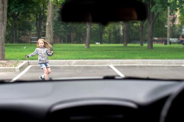 Young girl seen through windscreen running in front of car