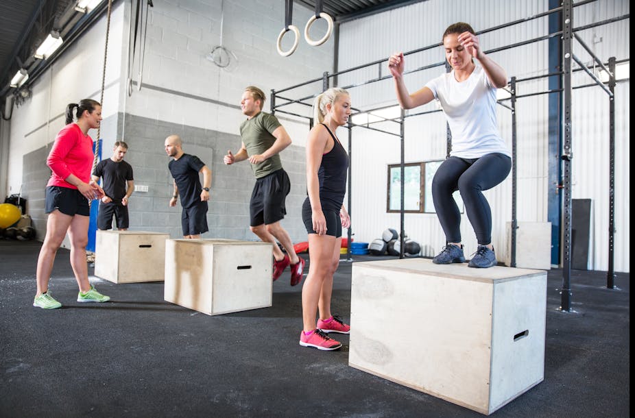 A group of people in a gym perform box jumps as part of Crossfit training.