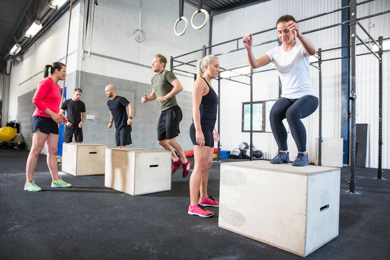 A group of people in a gym perform box jumps as part of Crossfit training.