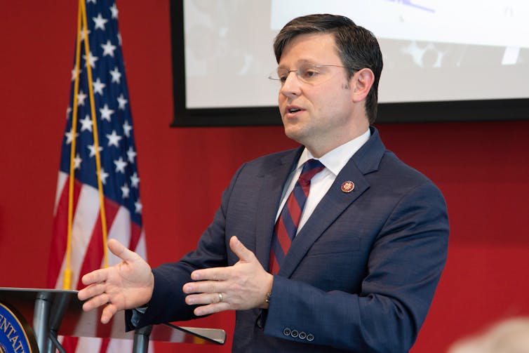 A man in a suit stands by a US flag