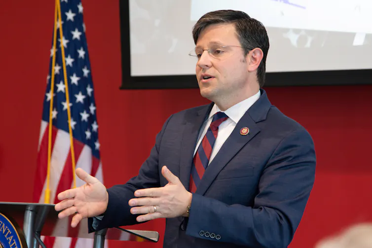 A man in a suit stands by a US flag