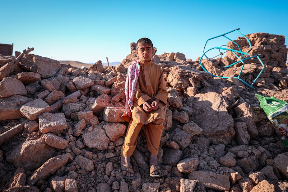 Enfant afghan assis sur les débris d'une maison.