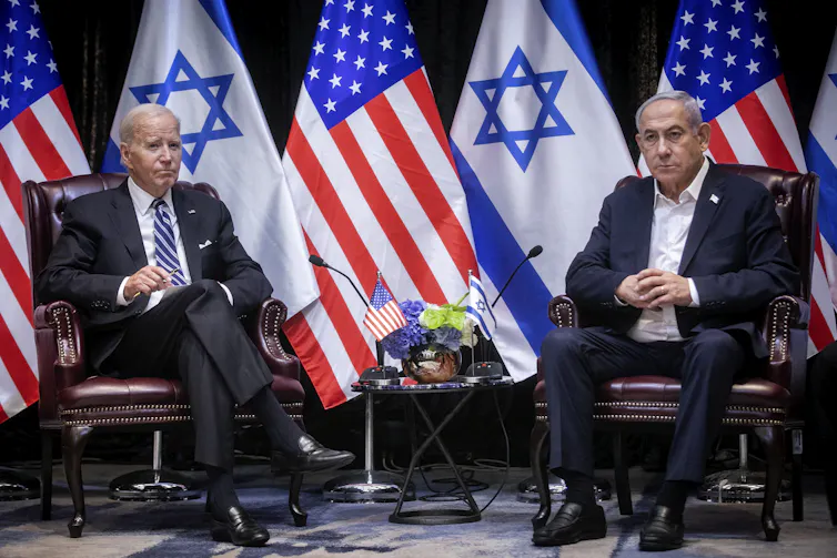 US president Joe Biden sits with Israeli pprime minister Benjamin Netanyahu in front of their national flags.