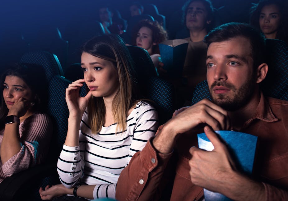 Trois jeunes adultes regardent un film dans une salle de cinéma.