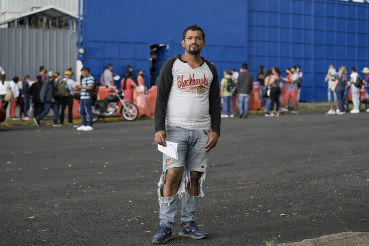 A man in a Blackhawks polo shirt and ripped jeans holds papers.