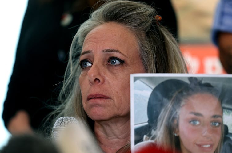 A worried and teary-eyed woman holds a photo of her daughter.