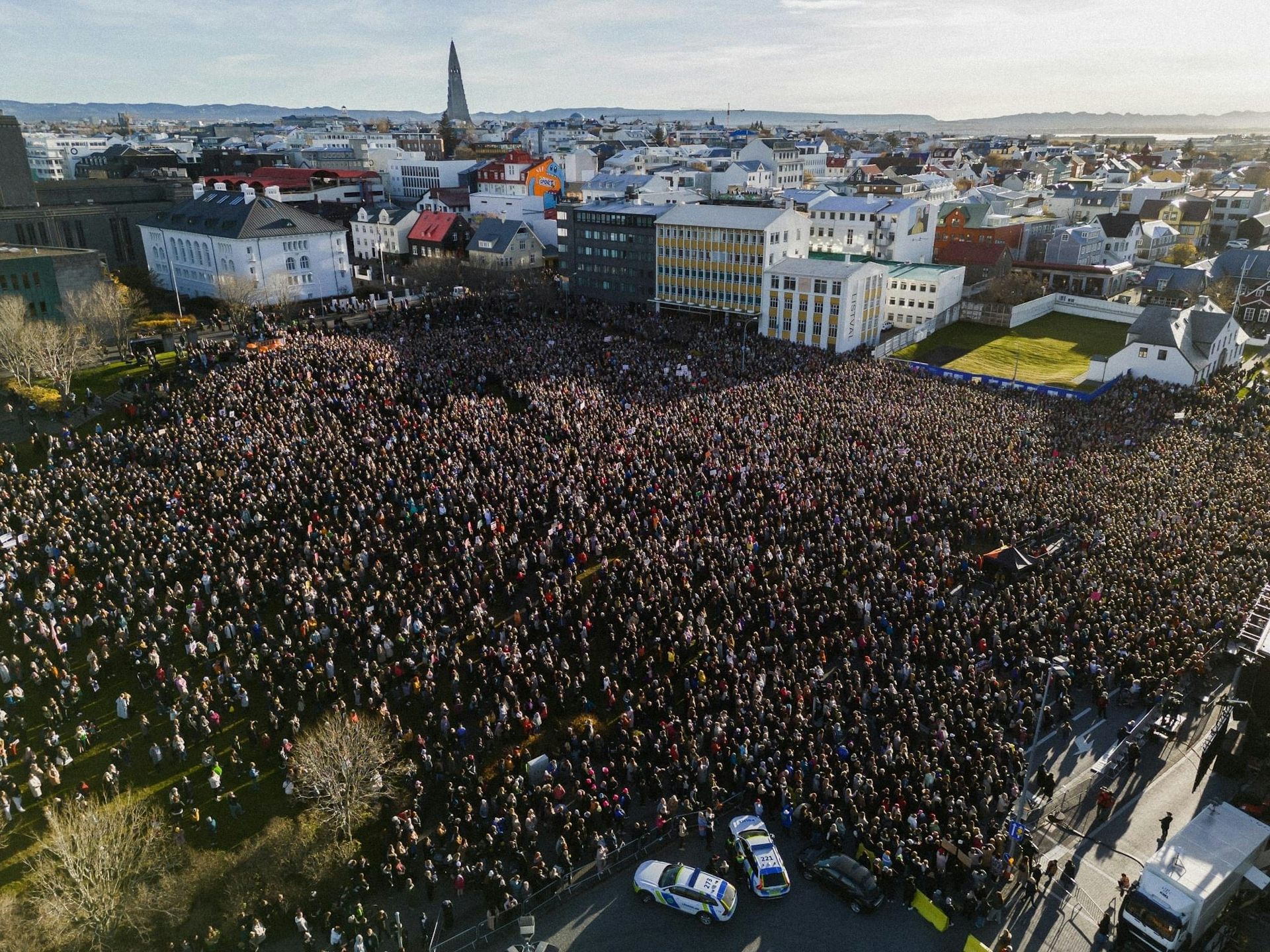 Aerial shot of a large crowd of people gathered in an open space with a small city backdrop.