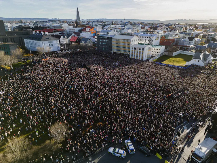 Aerial shot of a large crowd of people gathered in an open space with a small city backdrop.