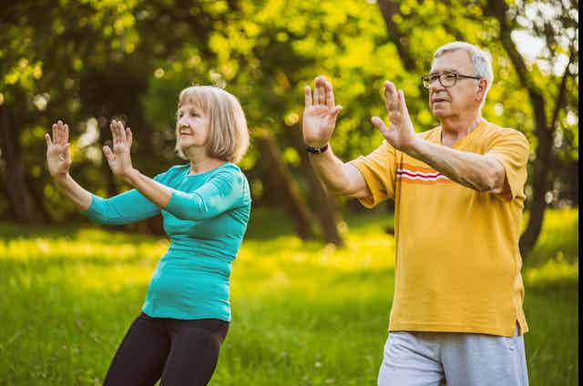 An elderly couple practice tai chi outdoors.