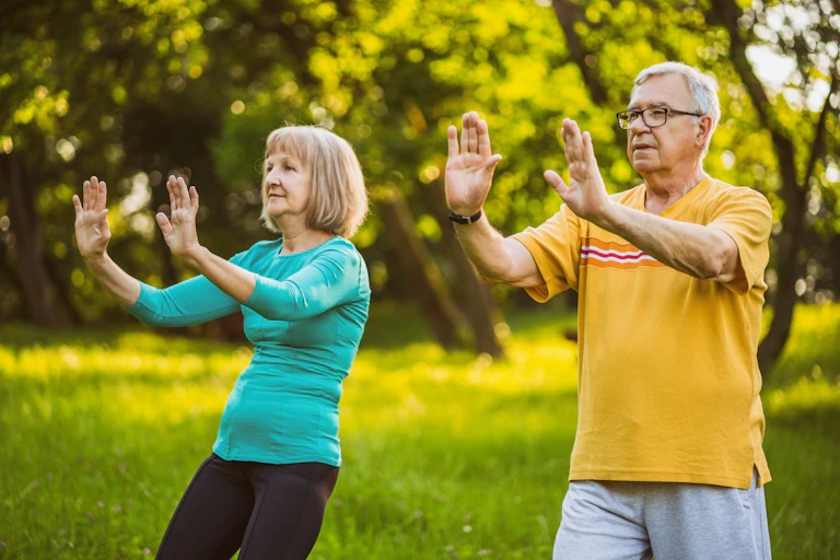 An elderly couple practice tai chi outdoors.
