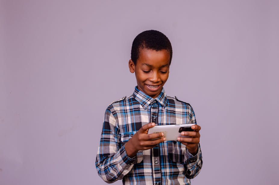 A photograph of a young boy in a plaid shirt holding a cell phone on a purple background