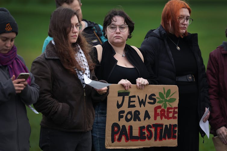People wearing black clothes stand in front of a sign reading 'Jews for a free Palestine.'