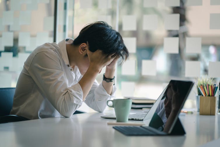 A person sitting a desk with their head in their hands