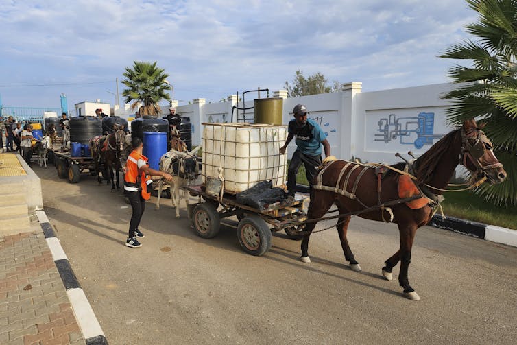 A line of large containers on wagons, one pulled by a horse