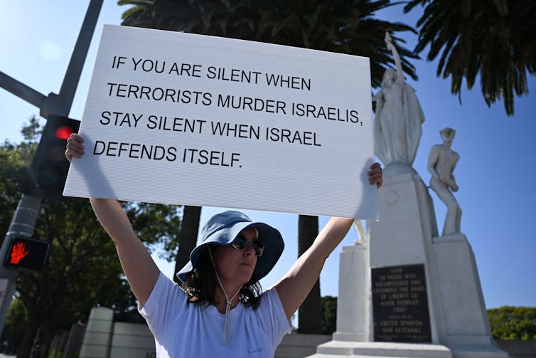 A person holds a sign reading 'If you are silent when terrorists murder Israelis, stay silent when Israel defends itself.'