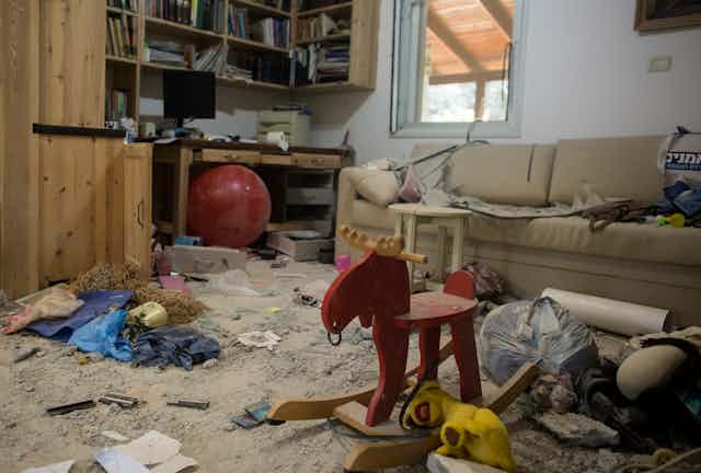 A living room with children's toys and a couch sits partially destroyed and covered in dust and rubble.