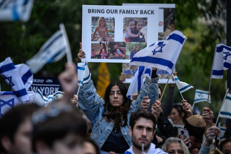 A crowd of people stand, with one person holding a sign saying 'Bring our family back' with photos of people below the words.