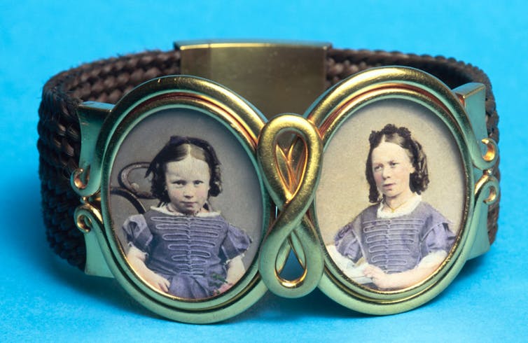 A cuff bracelet with photographs of two young girls, photographed against a turquoise background.