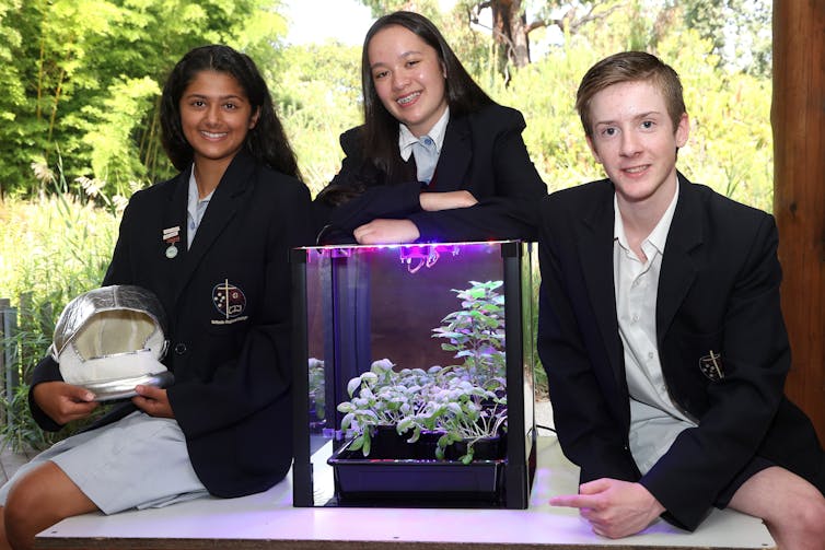 A photo of three Catholic Regional College students posing with a plant inside a growth chamber.