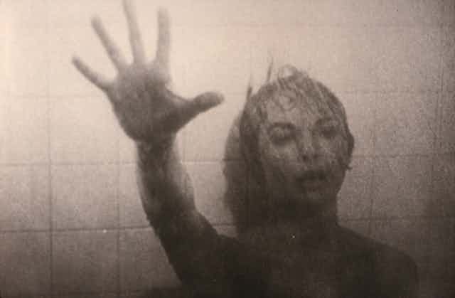 Escena de Psicosis en la que una mujer extiende el brazo buscando ayuda mientras su cuerpo se desliza por las baldosas de la pared.