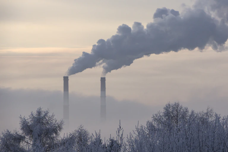 Two smokestacks spewing smoke on a misty winter horizon.