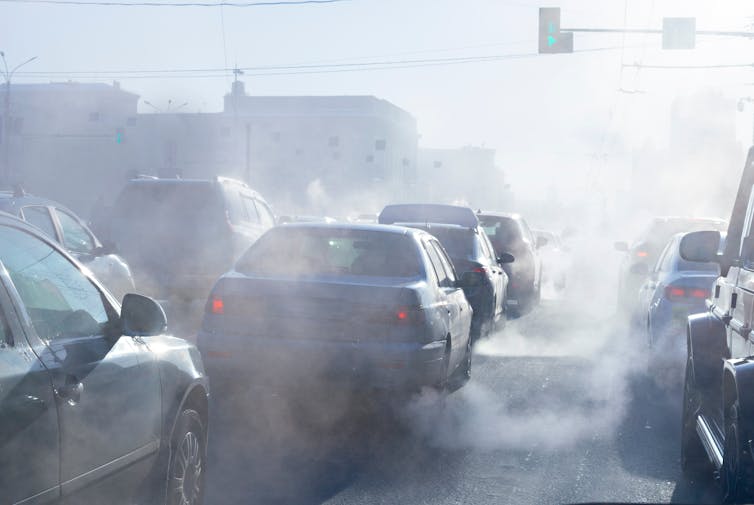 Cars surrounded by exhaust fumes in traffic.