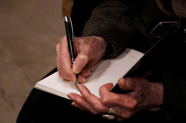Unas manos ancianas sostienen un bolígrafo antes de escribir en la página en blanco de un libro.