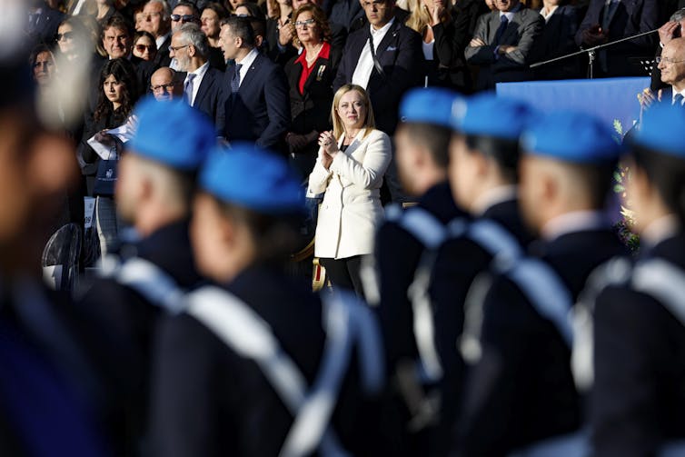 Giorgia Meloni stands in the background as troops stand to attention in the foreground.