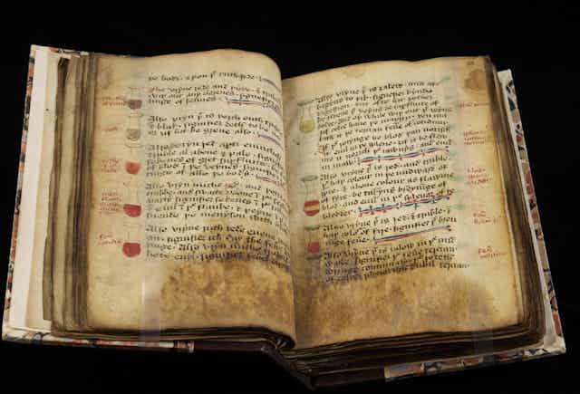 Ancient book with yellowed, stained pages open to a section of illustrated multicolor flasks lining the margins with blocks of handwritten text alongside