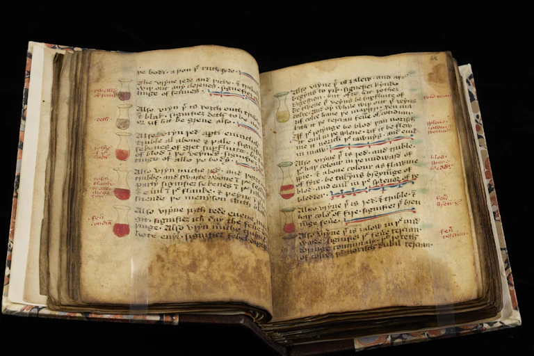 Ancient book with yellowed, stained pages open to a section of illustrated multicolor flasks lining the margins with blocks of handwritten text alongside