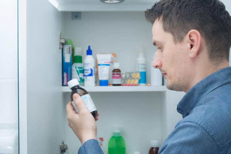 Man looks at medicine bottle in front of cabinet
