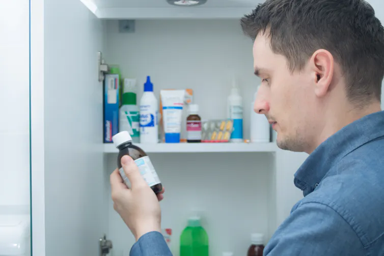 Man looks at medicine bottle in front of cabinet