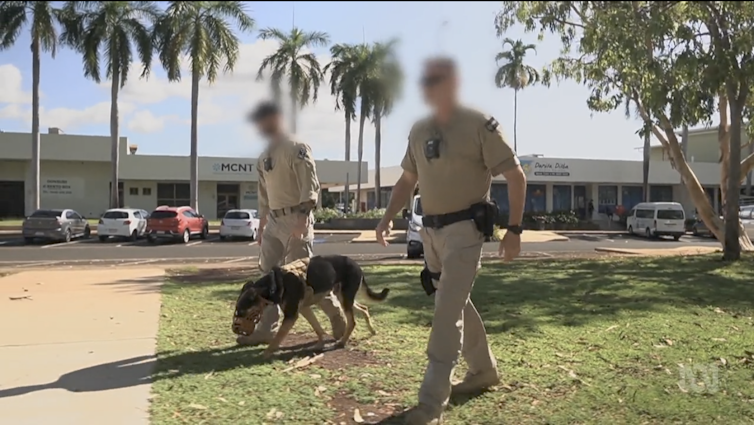 Two security officers walk with a dog with a muzzle.