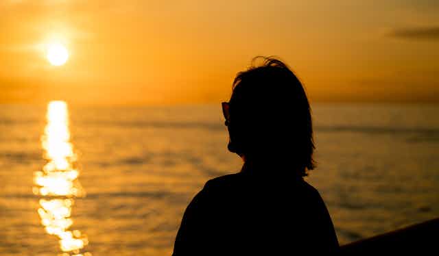 Woman looks at sun above the horizon