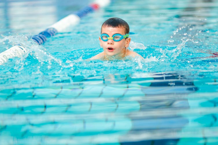 A boy wearing goggles swims in a swimming pool.
