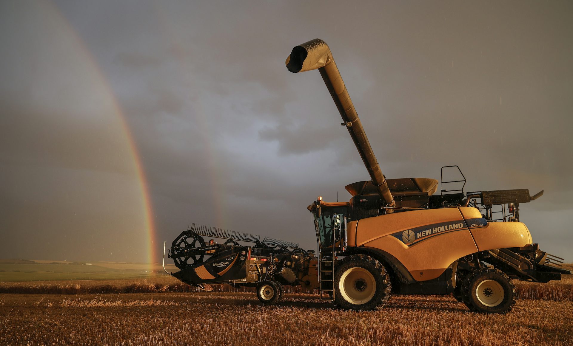 A rainbow behind a wheat harvesting combine machine.