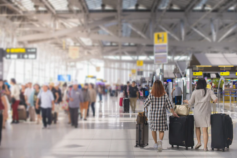 Two women carrying their luggage through an airport terminal.