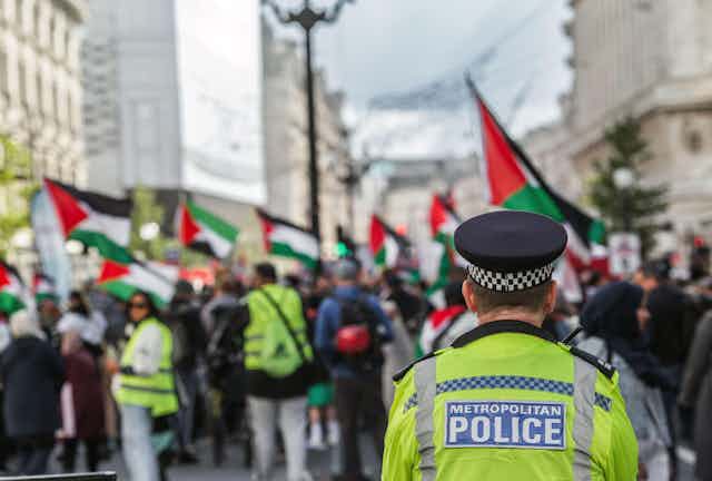 A Met police officer looks on at a crowd of people waving Palestinian flags