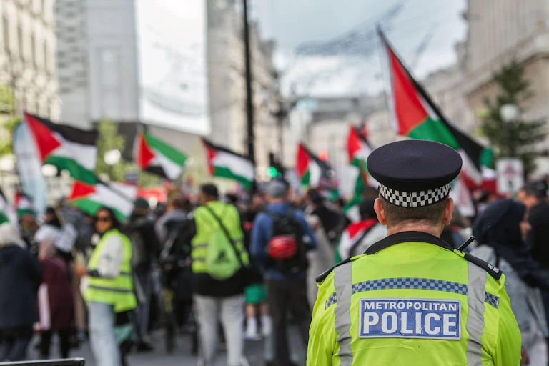 A Met police officer looks on at a crowd of people waving Palestinian flags