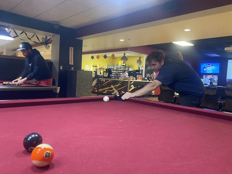 A young adult male takes a shot on a red velvet pool table.