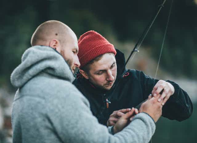 two men handling a fishing hook on a line